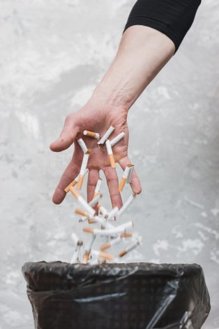 hand throwing cigarettes trash against old wall scaled